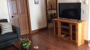 Una sala de estar con una mesa de centro de madera, un sofá, un televisor sobre un mueble de madera y una decoración de montaña en la pared.
