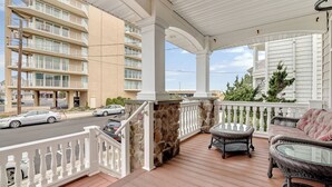 Un espace extérieur abrité, doté d’un mur en pierre, d’une balustrade blanche, de meubles en osier et offrant une vue sur un immeuble à plusieurs étages en arrière-plan.