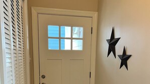 Un couloir avec une porte blanche, un plancher en bois et deux décorations en forme d’étoile sur le mur.