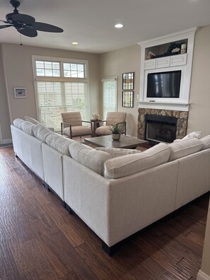 A living room with a sectional sofa, two armchairs, a coffee table, a fireplace, and a TV mounted above it.