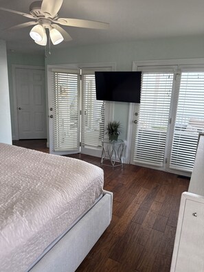 A bedroom with a bed, a ceiling fan, a TV, and a sliding door with blinds.