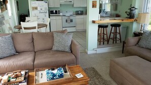 A living room with a sofa, a coffee table with board games, and a kitchen area with white cabinets and a microwave. - The Guest Cottage in Paradise. (Northwood)