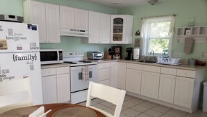 A kitchen with white cabinets, a stove, a microwave, and a dining table with placemats. - The Guest Cottage in Paradise. (Northwood)