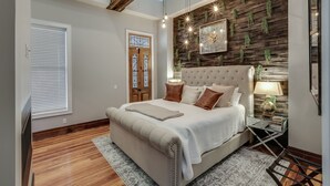 Un dormitorio con una cama grande, suelo de madera, un muro decorativo y una araña.