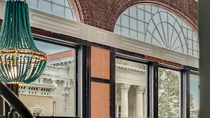 Vista a través de una ventana que muestra un candelabro verde decorativo, un arco de ladrillo y columnas de estilo clásico.