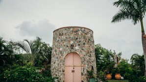 A stone tower with a pink door, surrounded by lush greenery and palm trees. - Heaven's Gate - Off Grid Ocean View Villa (Coral Bay)