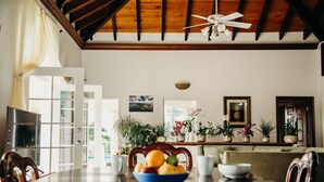 A dining area with a wooden table, chairs, a bowl of fruit, potted plants, and a ceiling fan. - Heaven's Gate - Off Grid Ocean View Villa (Coral Bay)