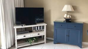 A room with a TV on a white entertainment unit, a blue cabinet with drawers, and a ship model lamp. - Self Checkin/Out | Family Friendly | Perfect Location | Free WiFi  (Miramar Beach)