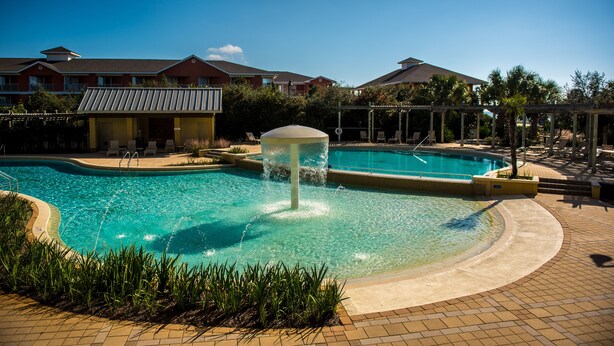 A swimming pool with a water feature in the center, surrounded by lounge chairs and a covered area with umbrellas. - Self Checkin/Out | Family Friendly | Perfect Location | Free WiFi  (Miramar Beach)