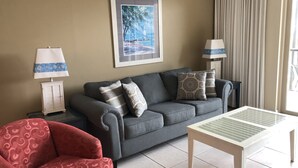 A living room with a grey sofa, patterned cushions, a red armchair, a white table, and a framed picture on the wall. - Self Checkin/Out | Family Friendly | Perfect Location | Free WiFi  (Miramar Beach)