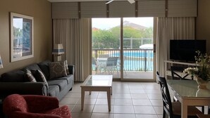 A living room with a sofa, a red chair, a glass table, a ceiling fan, and a TV. - Self Checkin/Out | Family Friendly | Perfect Location | Free WiFi  (Miramar Beach)