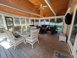 A covered outdoor area with a glass enclosure, wicker furniture, and a ceiling fan.
