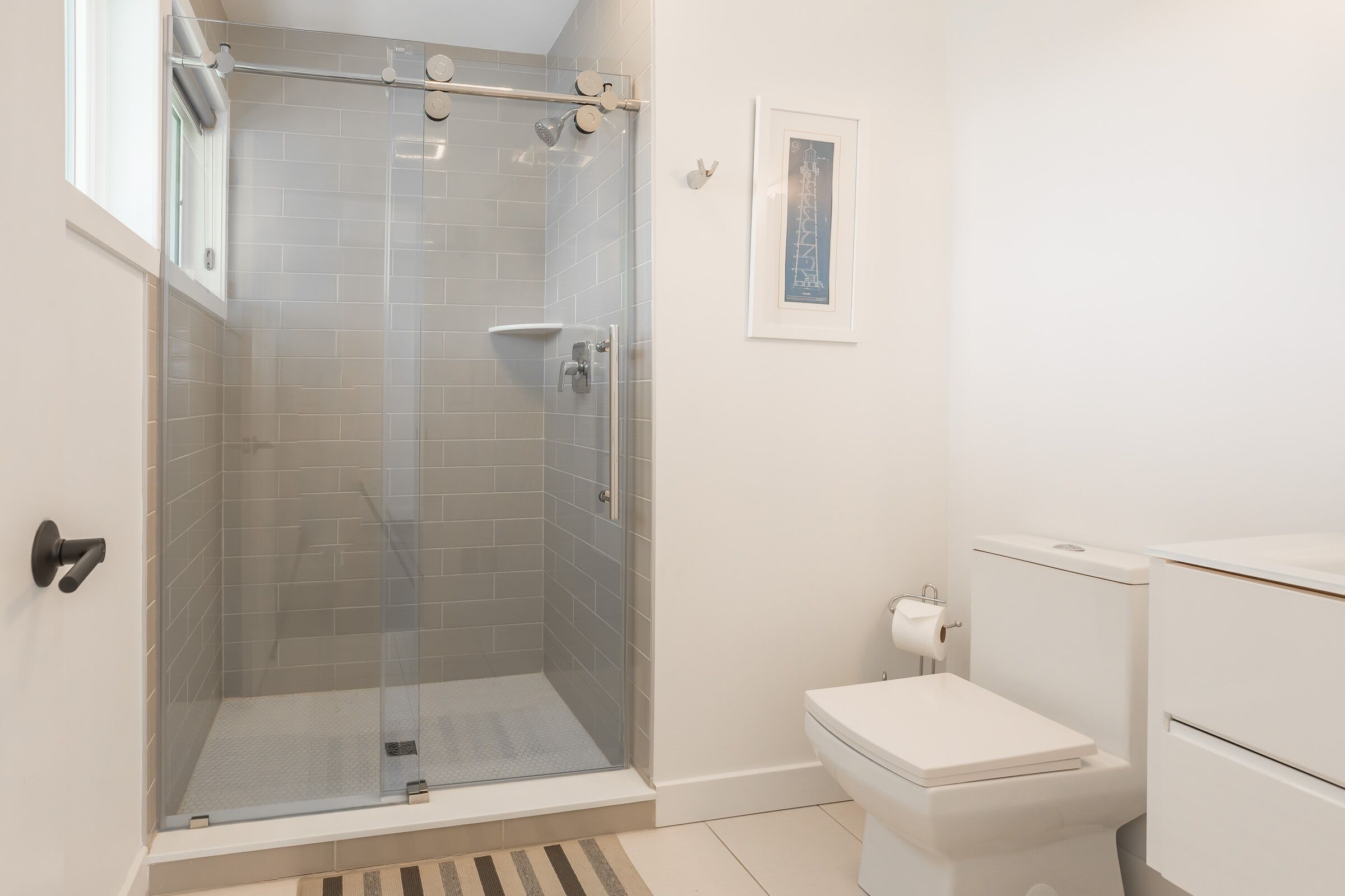 A modern bathroom with a glass-enclosed shower, a toilet, and a small sink.