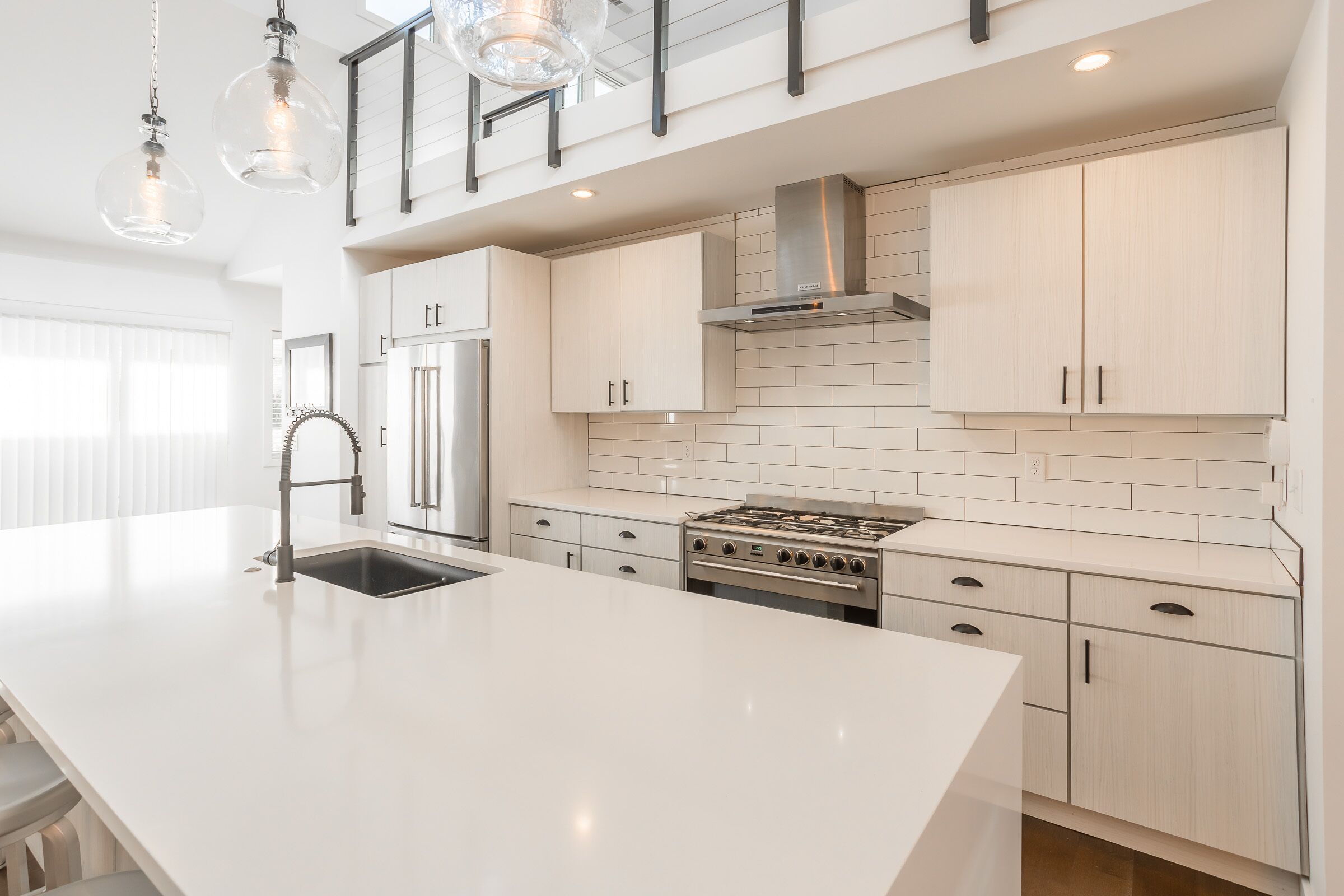 Une cuisine moderne avec des meubles blancs, un îlot central, des appareils en acier inoxydable et des luminaires suspendus.