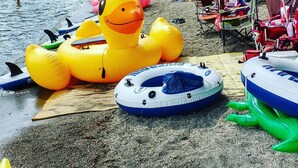 En strand med oppustelige legetøj, en træterrasse og udsigt til vand og bakker i baggrunden.