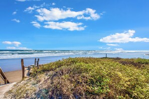 A beach with a wooden walkway leading to the water, surrounded by dense vegetation. - Beach Retreat Townhome | 3 Balconies, Beach Views & Heated Pool (Corpus Christi)