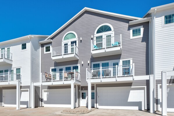 A multi-story residential building with two-story balconies, white garage doors, and a clear blue sky.