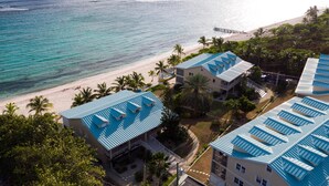 Une propriété située en bord de mer, comprenant plusieurs bâtiments aux toits bleus, une plage et des palmiers.