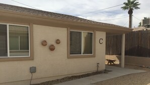 A single-story house with a beige exterior, two windows with blinds, a small porch area, and a wooden fence in the background. -   Casita 3 blocks from downtown!  Very clean ! (Wickenburg)