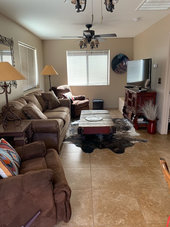A living room with a brown leather sofa, a wooden coffee table, a ceiling fan, and a television on a wooden stand.