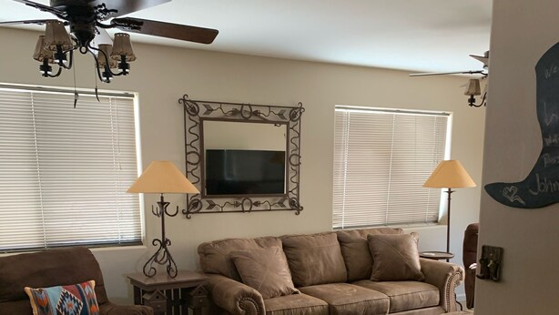 A living room with a brown leather couch, a wooden dining table with chairs, a ceiling fan, and a decorative mirror. -   Casita 3 blocks from downtown!  Very clean ! (Wickenburg)