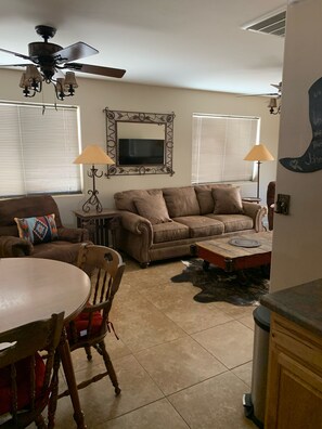 A living room with a brown leather couch, a wooden dining table with chairs, a ceiling fan, and a decorative mirror. -   Casita 3 blocks from downtown!  Very clean ! (Wickenburg)