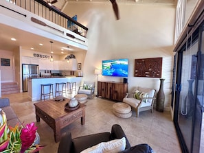 A spacious living area with a kitchen, a dining area, and a high ceiling with exposed beams.