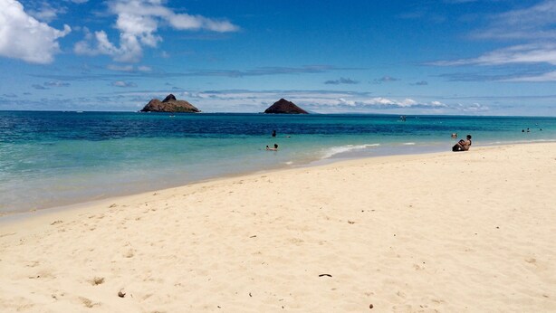 Una playa con agua azul cristalina, una orilla arenosa y dos imponentes formaciones rocosas al fondo.