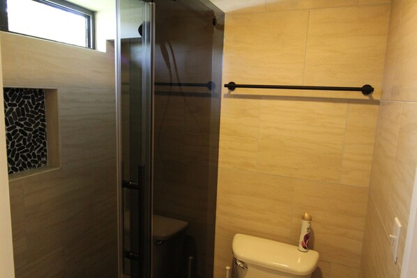 A bathroom with a glass shower enclosure, a toilet, and a towel rack.