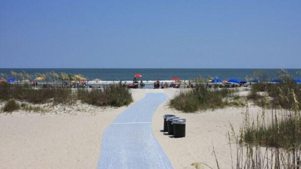 Ein Strandweg führt zum Meer, mit Strandsonnenschirmen und Mülleimern.