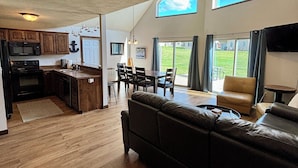 A spacious living area with a large sofa, a dining table, and a kitchen area with wooden cabinets and a microwave. - Cozy Okoboji Vacation Home At Bridges Bay Resort - backs to pool! #118 (Arnolds Park)