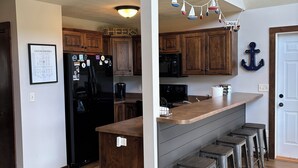 A kitchen with wooden cabinets, a black refrigerator, a wooden island with bar stools, and a ceiling fan. - Cozy Okoboji Vacation Home At Bridges Bay Resort - backs to pool! #118 (Arnolds Park)