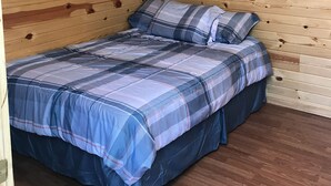 Una habitación pequeña y acogedora con paredes de madera y una cama con ropa de cama azul.
