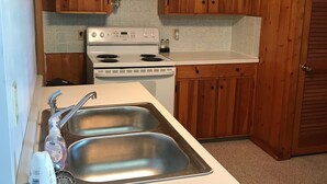 Una cocina con armarios de madera, una encimera blanca, un fregadero de acero inoxidable y una estufa blanca.