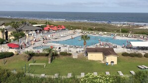 Ett poolområde med flera pooler, solstolar och parasoller, omgivet av ett staket och med utsikt över havet.