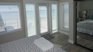 A hotel room with a bed, a desk, and a mirror. There are three doors with blinds, and a ceiling fan. - Any Closer to the Beach, You'd Have Sand in Your Sheets! After summer specials. (Miramar Beach)