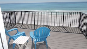 A wooden deck with two blue chairs and a white table, overlooking a beach with a metal railing. - Any Closer to the Beach, You'd Have Sand in Your Sheets! After summer specials. (Miramar Beach)