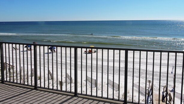 A beach view from a balcony with a railing, beach chairs, and umbrellas. - Any Closer to the Beach, You'd Have Sand in Your Sheets! After summer specials. (Miramar Beach)