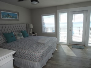 A bedroom with a large bed, a headboard, a nightstand with a lamp, and a window with blinds.