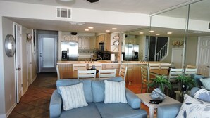 A modern kitchen with stainless steel appliances, a dining area with a blue sofa, and a large mirror reflecting the space. - Any Closer to the Beach, You'd Have Sand in Your Sheets! After summer specials. (Miramar Beach)