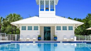Ein weißes Gebäude mit einem Pool davor. Es besitzt einen turmartigen Aufbau mit Fenstern und einer Tür mit der Beschriftung 'Restrooms'.