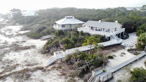 Une propriété située en bord de mer, comprenant une grande maison, plusieurs terrasses et un escalier en bois menant à la plage.