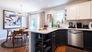 Une cuisine moderne dotée d’un îlot central, de meubles de rangement aux couleurs sombres et d’un coin repas avec des chaises et un tapis.