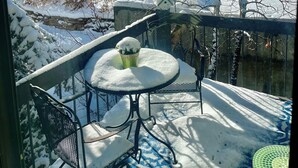 En snötäckt balkong med ett bord och stolar, med utsikt över ett snöigt landskap och en väg med en skylt som anger hastighetsbegränsningen.