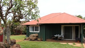 A small house with a red roof, a covered patio, and a lawn. - Plantation Style cottage short walk to beach and town 
Permit STPH2013/0004   (Paia)