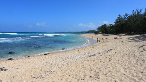 A sandy beach with clear blue water, some rocks near the shore, and a few people walking or sitting. - Plantation Style cottage short walk to beach and town 
Permit STPH2013/0004   (Paia)