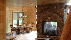 Un interior de madera con chimenea de piedra, comedor y televisor.