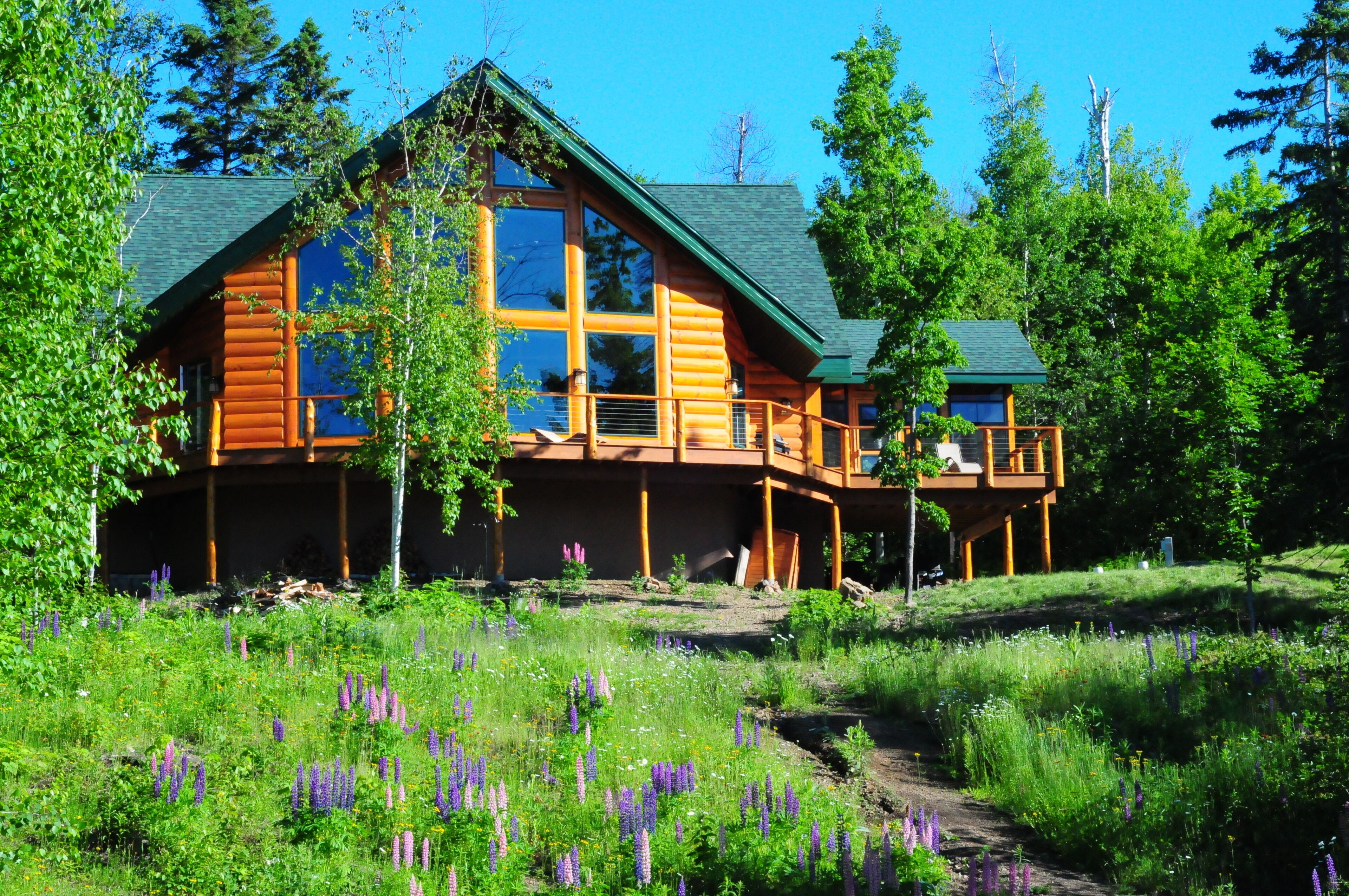 Une cabane en rondins avec un toit végétalisé, de grandes fenêtres et une terrasse.