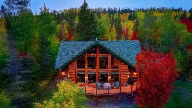 Una cabaña de troncos con terraza y ventanas grandes, rodeada de bosque.
