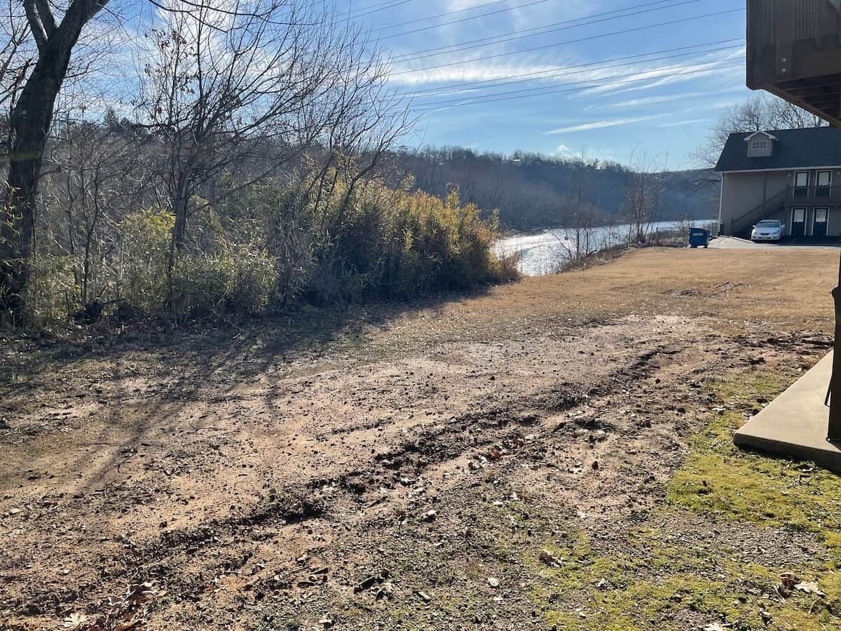 A dirt path leading to a house with a garage and a vehicle parked outside.